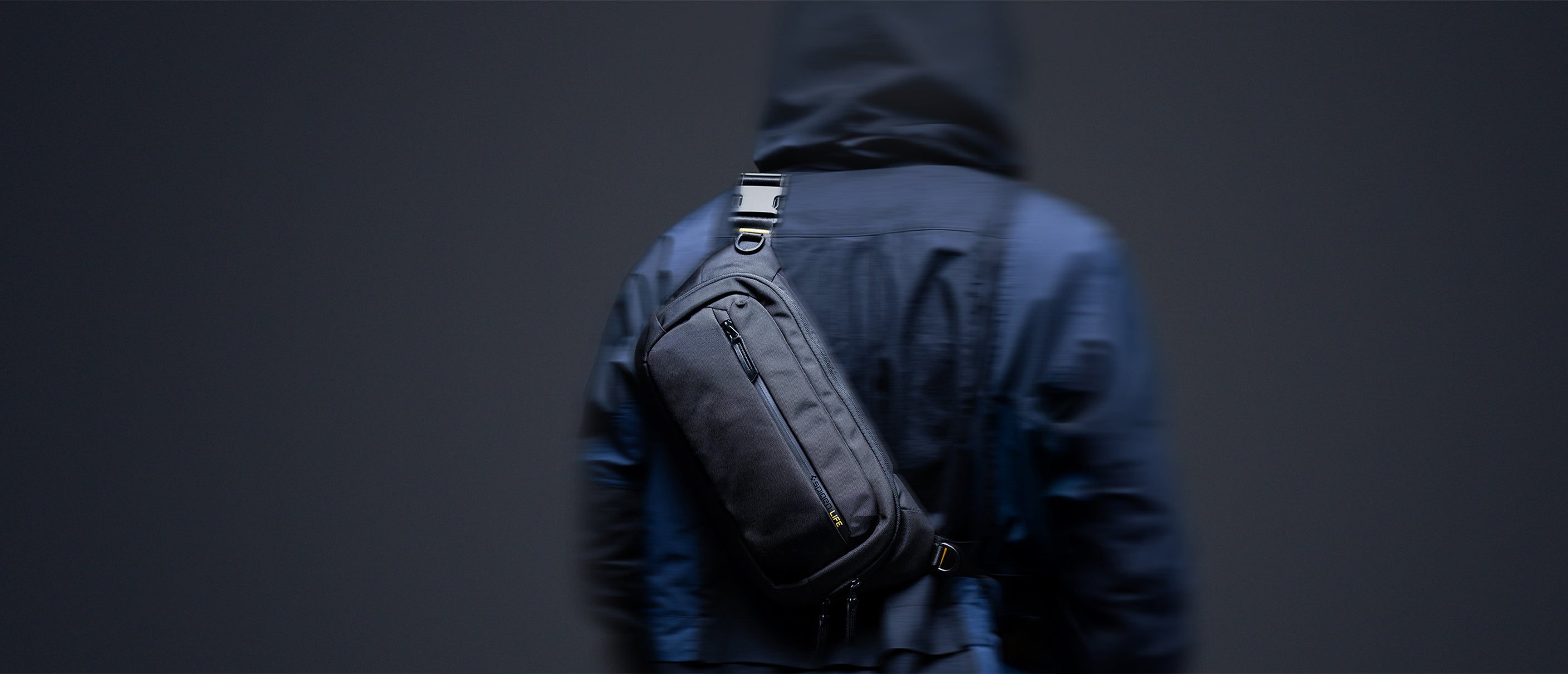 Showing person in navy jacket with hood up and carrying the Spigen Klasden Sling Bag