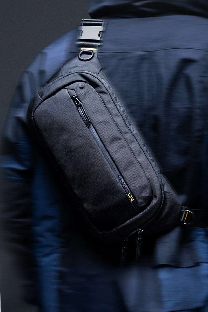 Showing person in navy jacket with hood up and carrying the Spigen Klasden Sling Bag