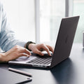 ACS11529 - MacBook Pro 14-inch Air Skin in Frost Black showing a person typing on a MacBook with the Frost Black case applied, placed on a desk in an office setting