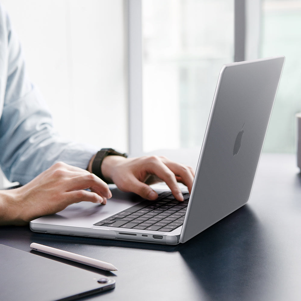 ACS11528 - MacBook Pro 14-inch Air Skin in Frost Clear showing a person typing on a MacBook with the Frost Clear case applied, placed on a desk in an office setting