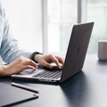 ACS11527 - MacBook Pro 16-inch Air Skin in Frost Black showing a person typing on a MacBook with the Frost Clear case applied, placed on a desk in an office setting