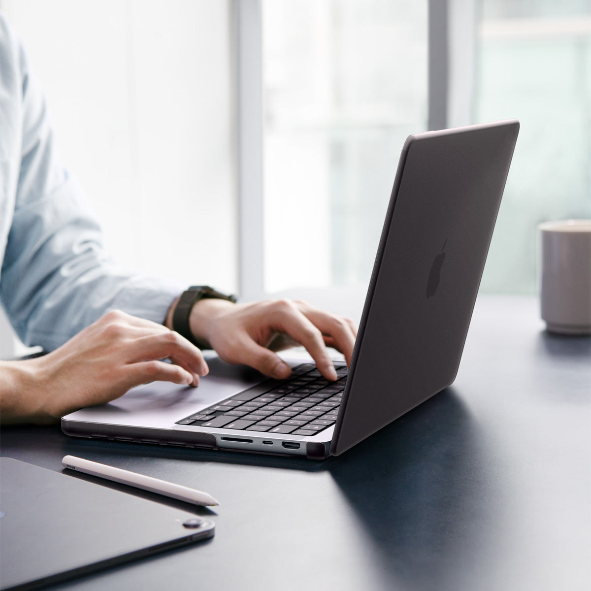 ACS11527 - MacBook Pro 16-inch Air Skin in Frost Black showing a person typing on a MacBook with the Frost Clear case applied, placed on a desk in an office setting