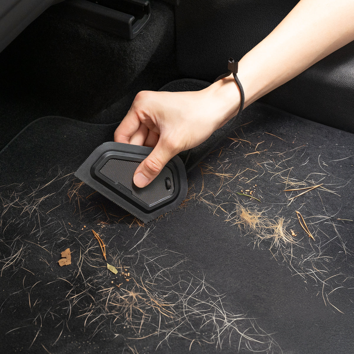 ACP11829 - Hand using the Spigen scraper to clear pine needles and debris from a car floor mat