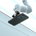 ACS09001 - Galaxy S25 Case Liquid Air in Abyss Green showing the robotic arm holding the device in an elevated horizontal position, angled slightly upward. Showing the device back facing outward, revealing its camera module. The robotic arm is positioned above a clean, structured background with defined panels