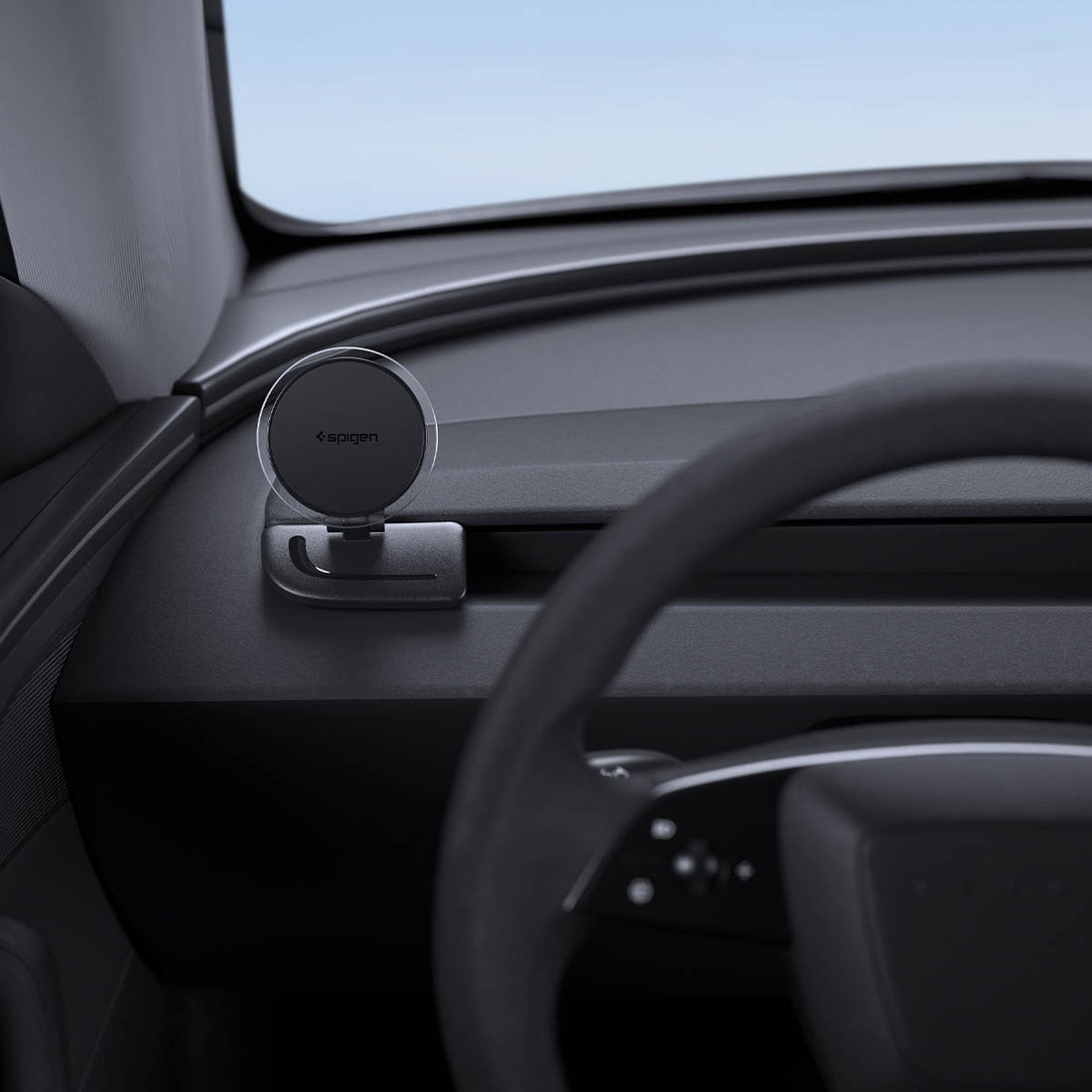ACP11873 - Spigen magnetic phone mount folded down on a car dashboard near the steering wheel, showing the Spigen logo on the magnetic plate