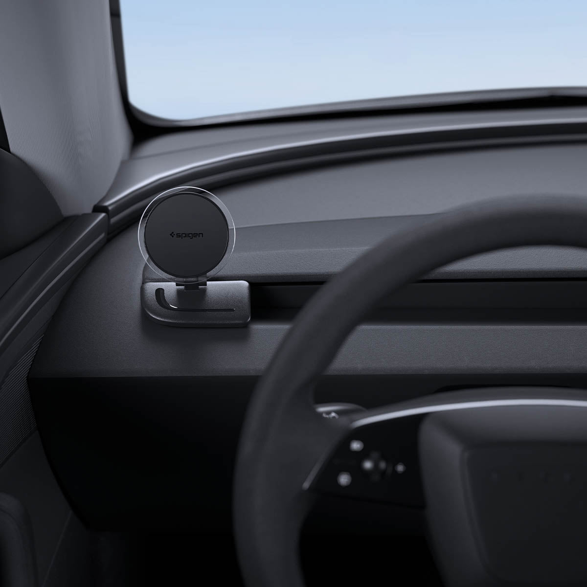 ACP11873 - Spigen magnetic phone mount folded down on a car dashboard near the steering wheel, showing the Spigen logo on the magnetic plate