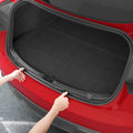 ACP11540 - Two hands pressing the Spigen bumper protector trim into both edges of an open Tesla trunk