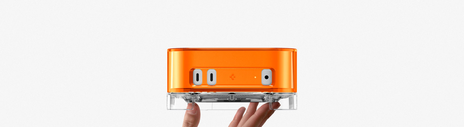 Hand holding Spigen Mac Mini Case Stand in orange from below showing front port cutouts and clear acrylic base
