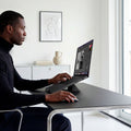 AMP11118 - Slim Fold Laptop Stand | Non-Adhesive | Black LD201-S9 showing side view of person using MacBook laptop propped up on laptop stand and using mouse