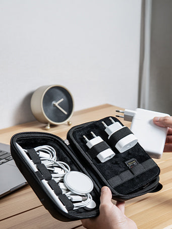 Showing hands holding a cable organizer with wall chargers and electronic cables.