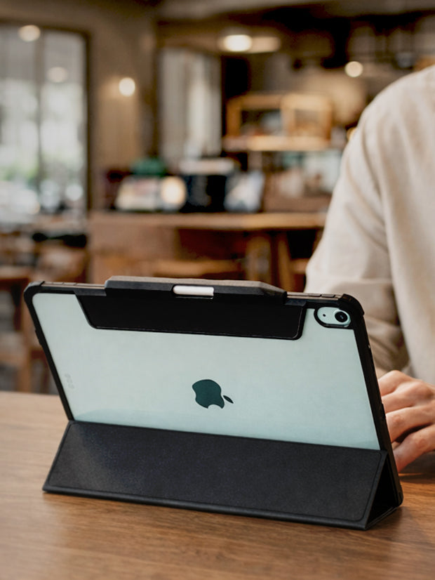 Spigen iPad Air Case propped in stand mode on wooden table with user working in cafe setting