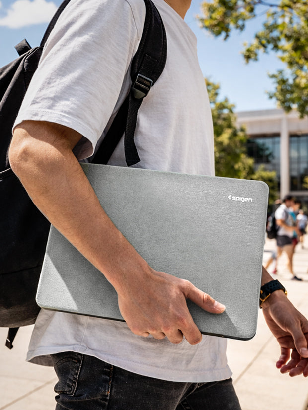 Spigen MacBook Sleeve carried under arm on campus walkway with backpack and students in background