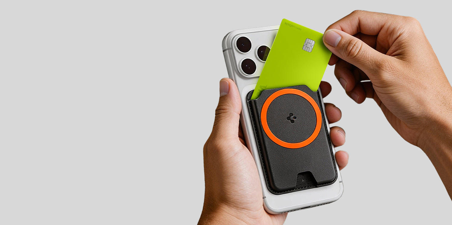 Hands pulling a card out of a Spigen MagSafe wallet in black with orange ring accent attached to the back of an iPhone
